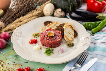 Steak Tartare with bread toasts and egg on blue wooden table