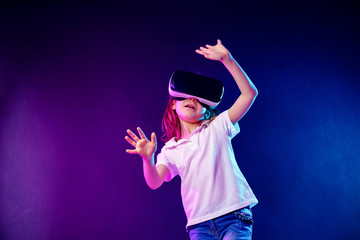 Girl 7 y.o. experiencing VR headset game on colorful background. Child using a gaming gadget for virtual reality. Futuristic goggles at young age. Virtual technology
