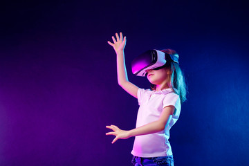 Girl 7 y.o. experiencing VR headset game on colorful background. Child using a gaming gadget for...