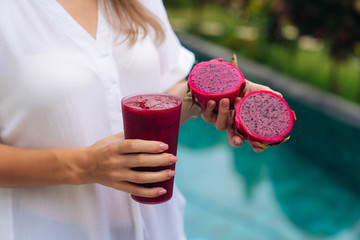 Close up glass of dragon fruit smoothie and fruit in woman hands
