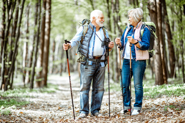 Beautiful senior couple hiking with backpacks and trekking sticks in the forest. Concept of active...