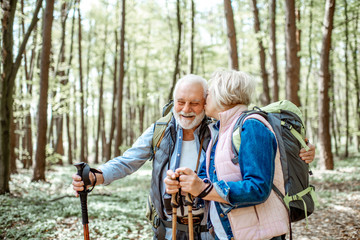 Beautiful senior couple hiking with backpacks and trekking sticks in the forest. Concept of active lifestyle on retirement