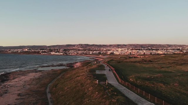 Aerial drone view of Paphos City and sunset mediterranean sea quay with pedestrians walking. Windy wavy sea and path along seashore.