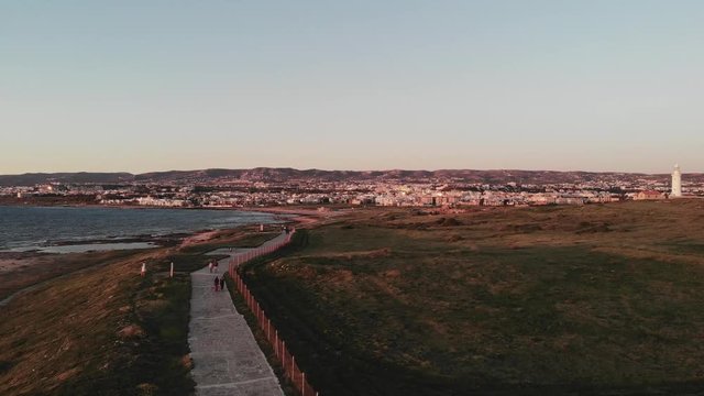 Aerial drone shot of pedestrian path along mediterranean sea with lighthouse in Paphos Cyprus