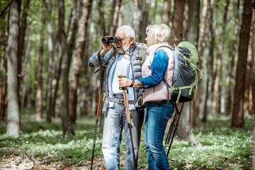 Senior couple looking with binoculars while hiking in the forest. Concept of an active lifestyle on retirement