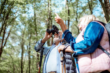 Senior couple looking with binoculars while hiking in the forest. Concept of an active lifestyle on retirement