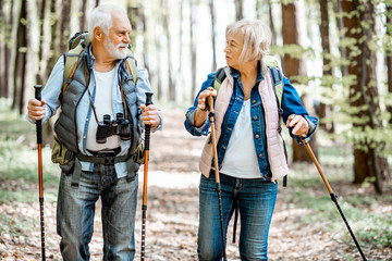 Beautiful senior couple hiking with backpacks and trekking sticks in the forest. Concept of an...