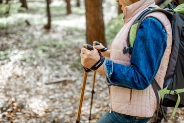 Senior woman hiking with trekking sticks in the forest, close-up view with cropped face