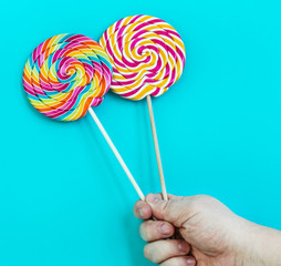 striped spiral multicolor Lollipop closeup in hand on blue background
