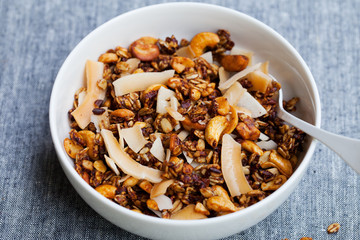 Healthy breakfast. Fresh granola, muesli with coconut, banana and nuts in a white bowl on grey background.