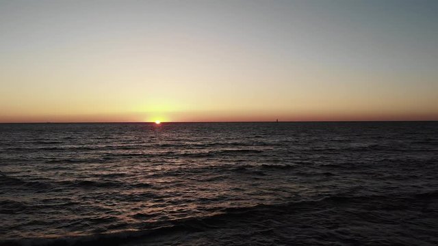 Red sun sets over ocean sea with waves with small black yacht boat in horizon. Sunset with sun path sun road towards the seashore.