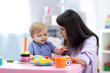 Obraz na płótnie Canvas Baby plays with mother or teacher in nursery or day care centre