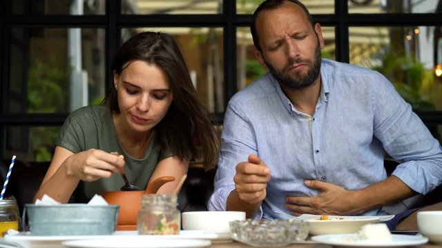 Couple eating meal in cafe in city, man having stomach ache