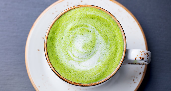 Matcha, green tea latte in a cup. Grey stone background. Top view.