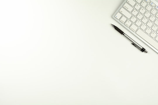 white keyboard and a pen on white desk background.