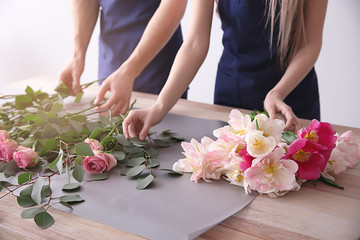 Obraz na płótnie Canvas Florists making bouquet at table against light background