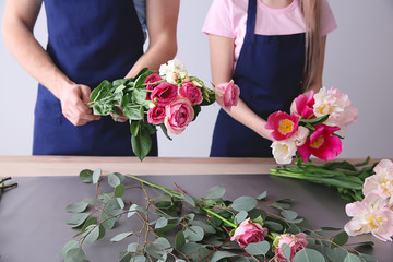 Florists making bouquet at table against light background
