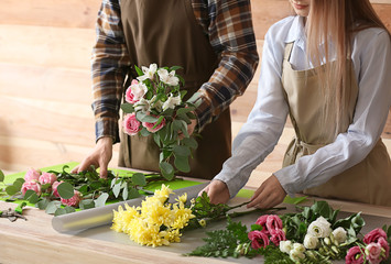 Florists making bouquet at table against wooden background