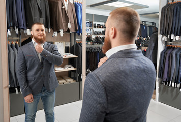 Happy strong man trying classic suit in clothes shop