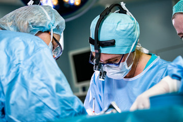 Surgeon and his assistant performing cosmetic surgery in hospital operating room. Surgeon in mask...