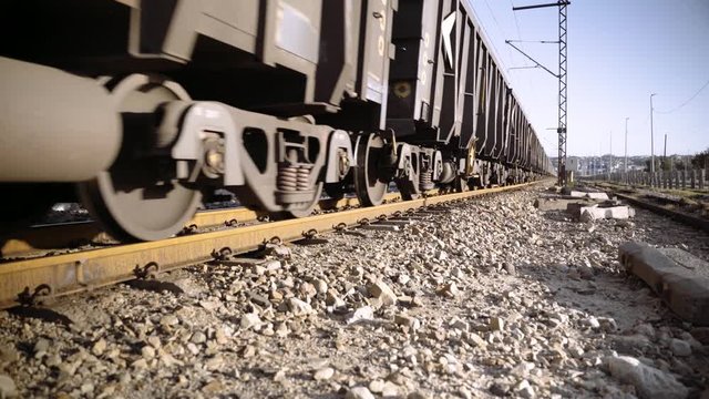 Wheels and wagons of an ore train on rail tracks pass by the camera into the distance.