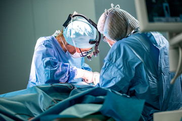 Surgeon and his assistant performing cosmetic surgery in hospital operating room. Surgeon in mask...