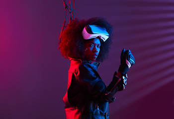 Curly dark haired girl dressed in a black leather jacket and gloves is wearing  the virtual reality...