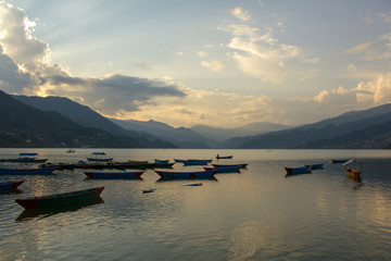 wooden old empty colored boats on the lake Phewa on the background of a mountain evening valley in the fog