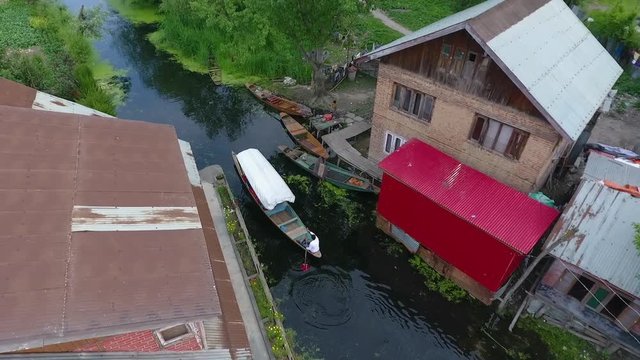 Drone, exterior, medium close up of a man paddling a boat on a creek through a neighborhood.
