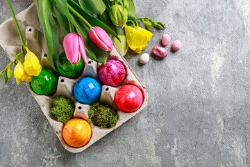Colorful Easter eggs in paper box and spring flowers in the background