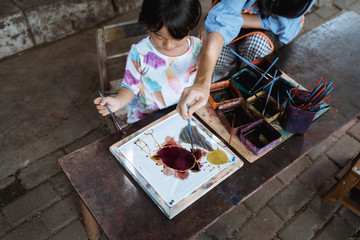 mother and child asian making batik pattern on white fabric