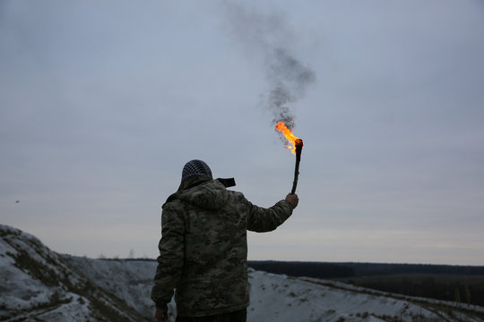 Soldier is holding torch with fire. Man in camouflage uniform and checkered keffiyeh shemagh bandana. Terrorist in the mountains gorge. War concept. White hills and dry grass in the desert.