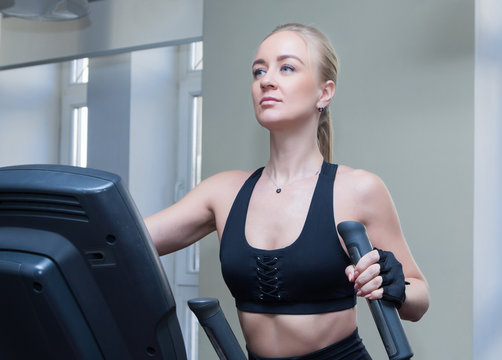 girls blonde with long hair in a black sports top and black leggings doing sports exercises for the leg muscles on the stepe in the sports hall