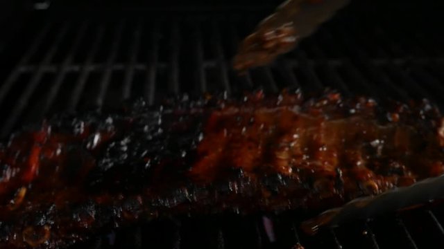 Turning over a rack of ribs on a grill using a pair of tongs