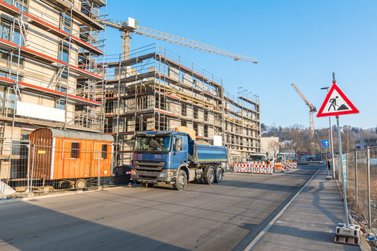 Rohbau eines Mehrfamilienhauses mit Baufahrzeugen, Ger&uuml;st und Baustellenschild