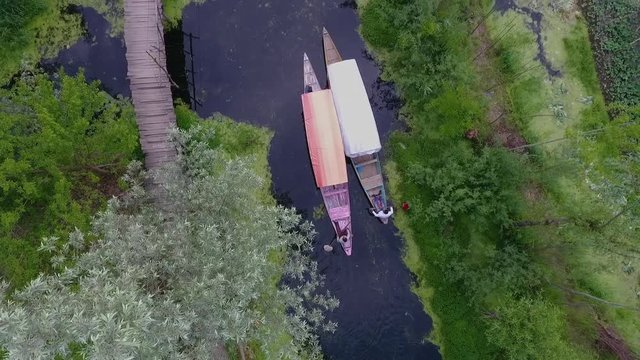 Drone, exterior, medium wide shot of two boats paddling through a creek alongside farmland.