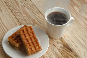 Hot coffee on a wooden stand with waffle, top view