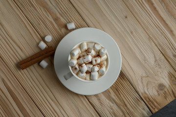 Hot morning coffee with marshmallow and cinnamon on a wooden stand, top view