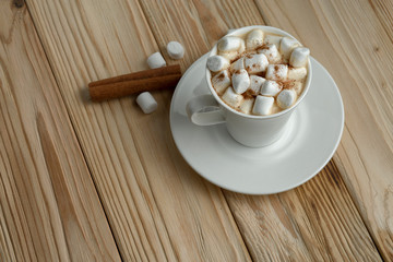 Hot morning coffee with marshmallow and cinnamon on a wooden stand, top view