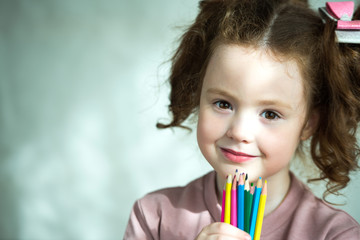 Portrait of little girl holding colored pencils and looking at camera