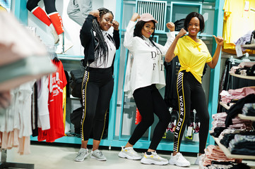 Three afican american women in tracksuits shopping at sportswear mall against shelves. Sport store theme.