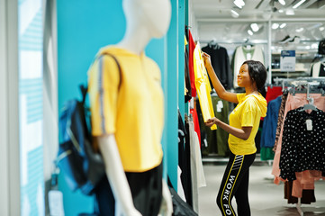 Afican american women in tracksuits shopping at sportswear mall against shelves. She choose yellow t-shirt. Sport store theme.