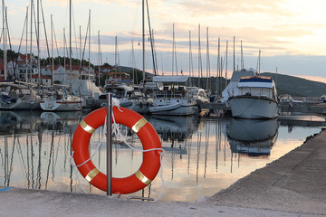 Orange life ring on the pier in the Croatian marina against the backdrop of sailing yachts. Safety...