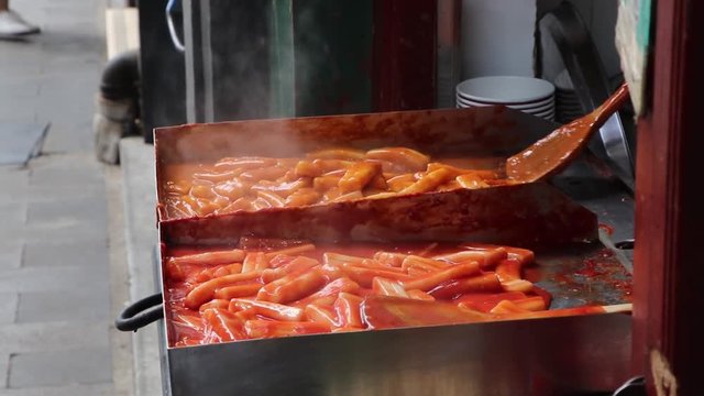 Medium shot as stirring fresh tteokbokki while frying it, street food vendor in China, Bejing