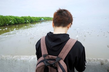 Back view of young travelers with backpacks are taking pictures of birds and river views in Samut...