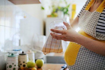 Close up of Caucasian pregnant woman wiping dish with dishcloth while standing in kitchen.