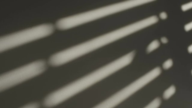Shadows of a closing window shutter on the white wall of a room