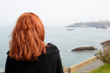 Fototapeta premium Woman enjoying the view of a sandy beach and white lighthouse in Biarritz, France.