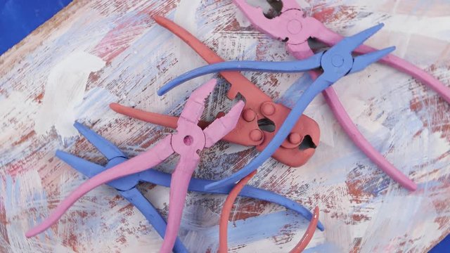 Composition of old metal pliers, painted in azure, pink, orange color, as an element of art design, on an abstract background