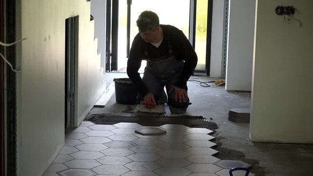 Handyman level glue with trowel and lay hexagon shape tiles on floor